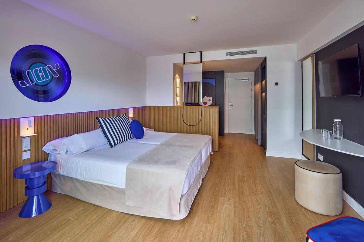 Una habitación de hotel moderna con cama, mesita de noche y un espejo redondo.