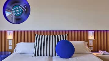 A hotel room with a bed, striped pillows, a blue pillow, and a wall-mounted light fixture.