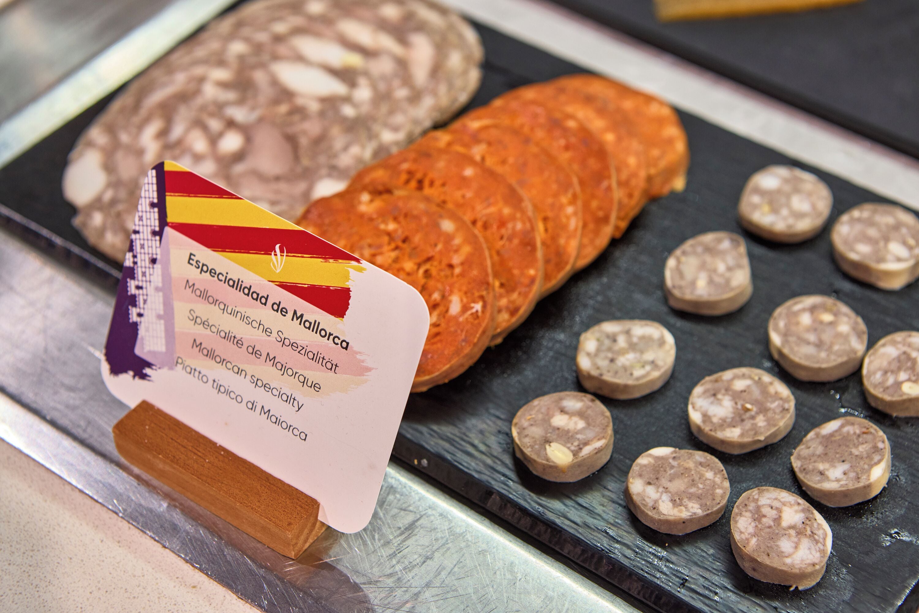 A display of various cured meats, including sliced salami and other types of salumi, arranged on a black slate board.