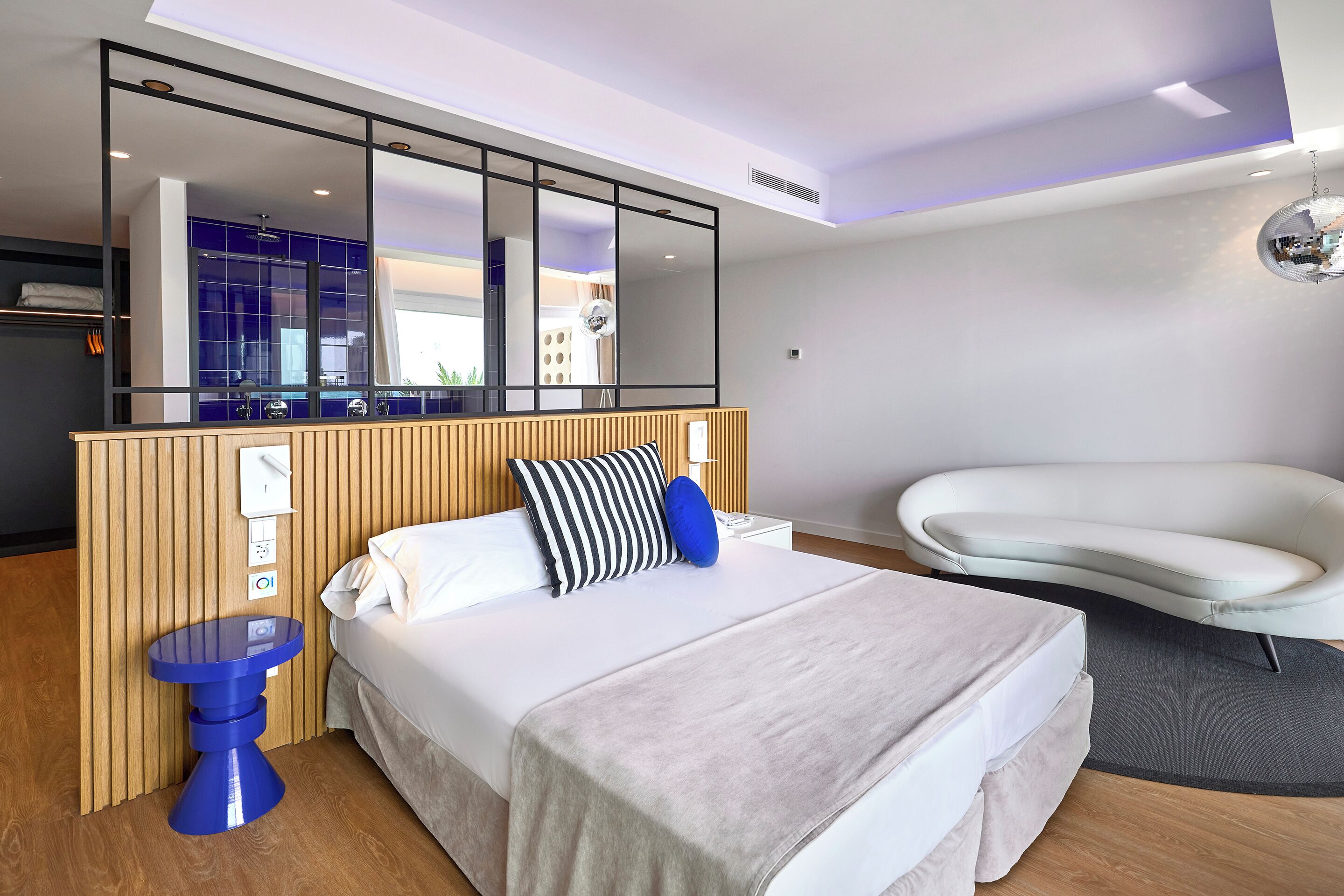 Habitación de hotel moderna con una cama grande, una mesita de noche, un espejo y una bañera blanca.