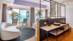 Una habitación de hotel moderna con un ventanal grande, un sofá, un escritorio con lavabo y un espejo.