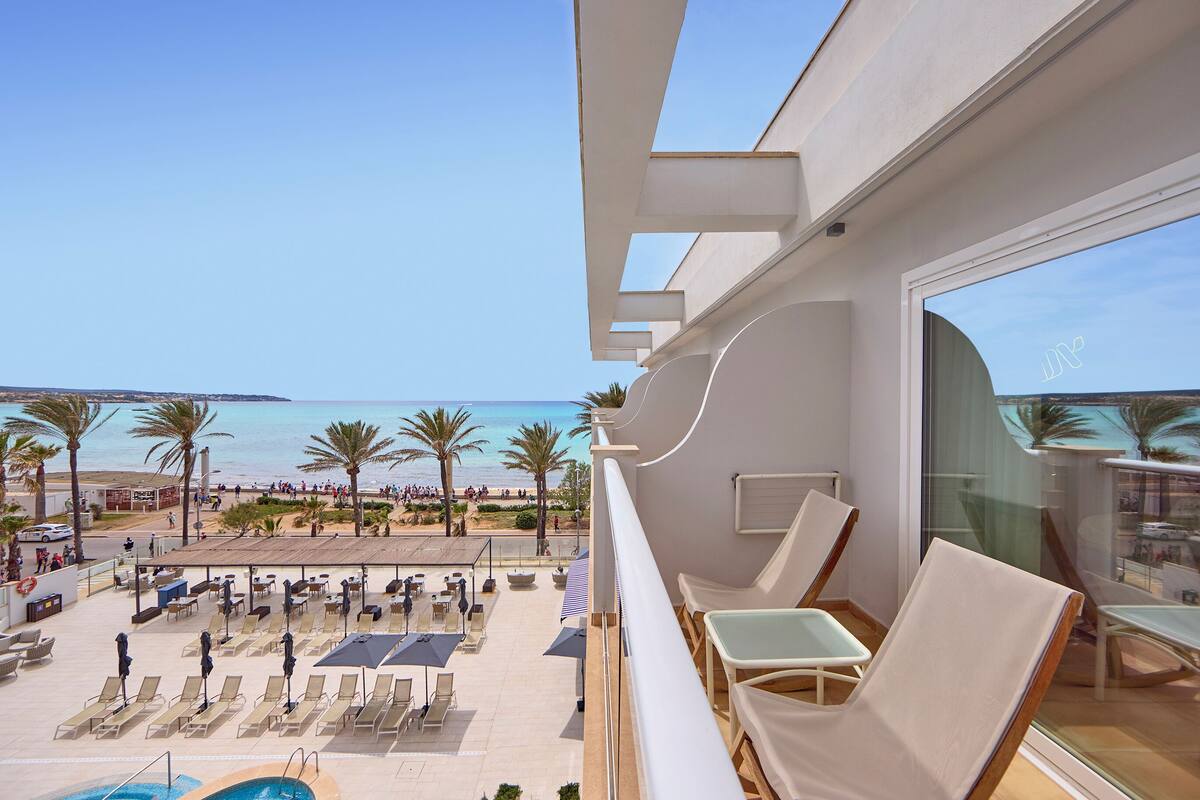 A balcony with a pool, lounge chairs, and a view of the beach and ocean.