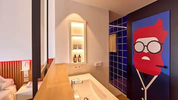 Une salle de bain moderne avec un meuble-lavabo en bois, un lavabo blanc et un miroir. On y trouve une étagère avec des articles de toilette et une serviette accrochée au mur.
