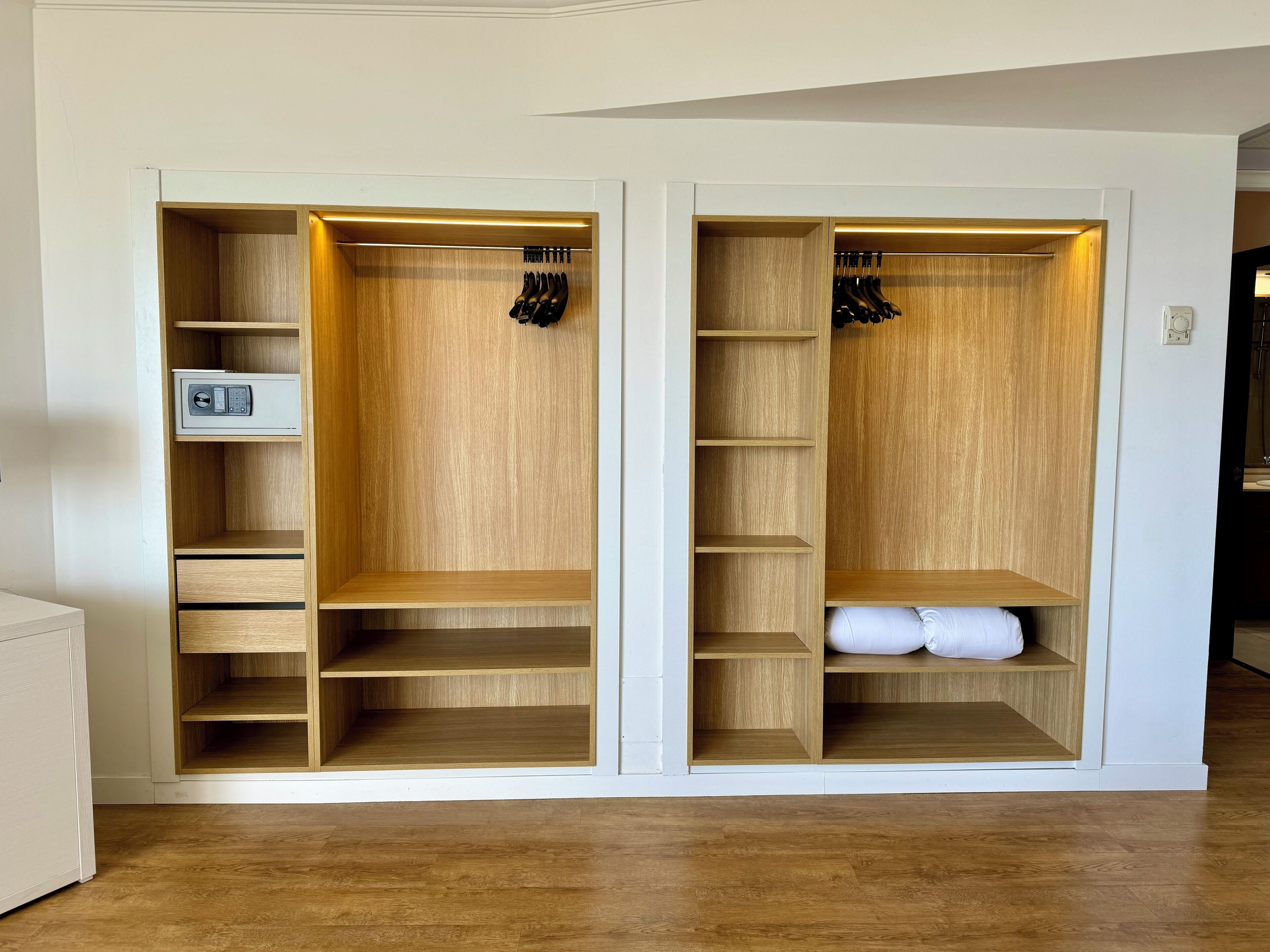 A walk-in closet with multiple shelves and hanging space, a built-in safe, and a padded bench.