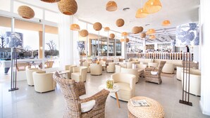 A spacious, well-lit lounge area with wicker furniture, large windows, and hanging wicker lamps. - Cabot Pollensa Park Spa - Family Resort (Pollenca)