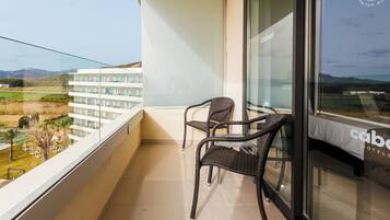 A balcony with wicker chairs, a glass table, and a view of a golf course and buildings.