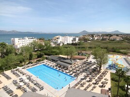 Un resort con una piscina grande, tumbonas y vistas al mar y a las montañas.