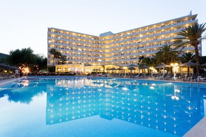 Un hotel grande con piscina, varios balcones y palmeras.