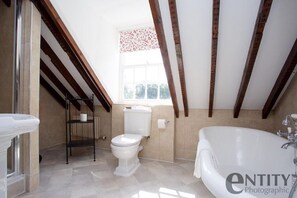 Une salle de bain moderne avec des toilettes blanches, une baignoire blanche et une fenêtre ornée d’un rideau à motifs floraux.