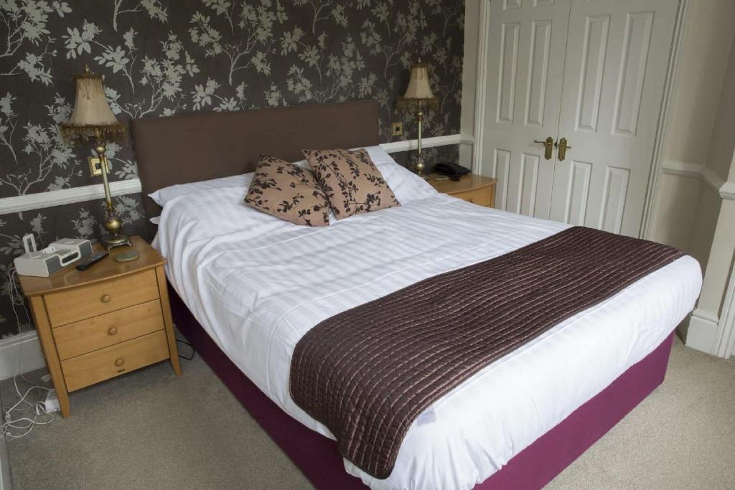 A neatly made bed with a white and brown striped blanket, two bedside lamps, and a wooden nightstand with a telephone and a lamp.