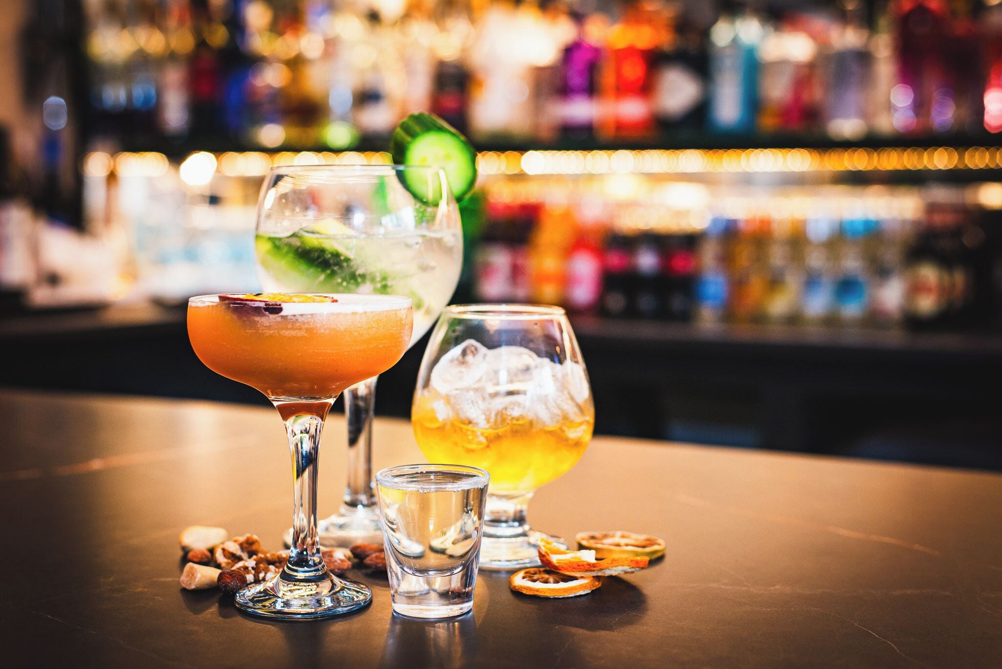Three cocktails on a bar counter with a blurred background of bottles.