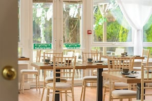 An indoor dining area with bamboo chairs and tables, a window with a view of greenery, and a door with a push bar sign.