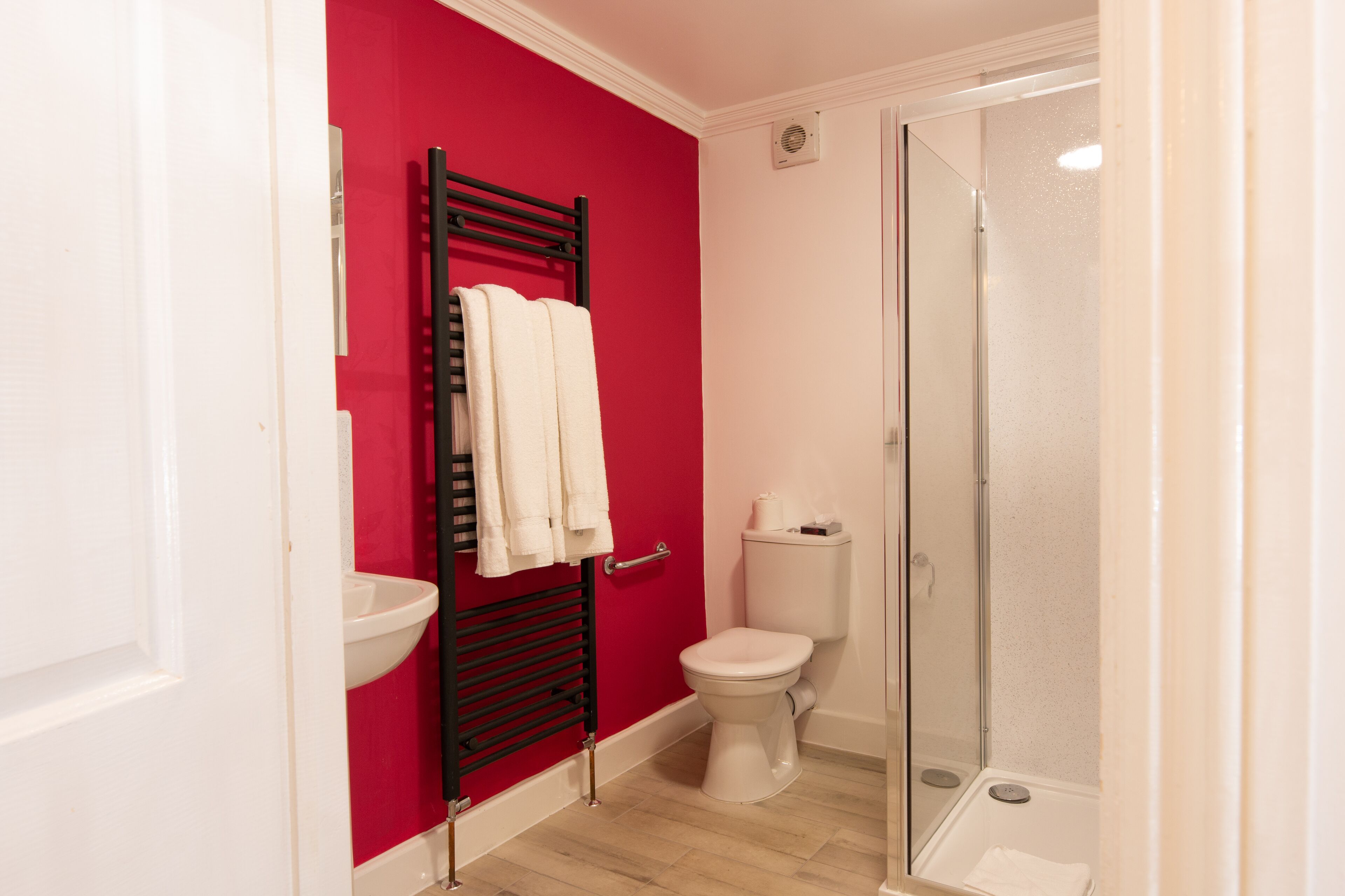 Un baño con una pared roja, un lavamanos blanco, un inodoro blanco y una ducha con cerramiento de vidrio.