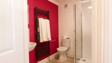 Un baño con una pared roja, un lavamanos blanco, un inodoro blanco y una ducha con cerramiento de vidrio.
