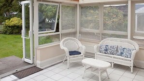 Un invernadero con mobiliario de mimbre blanco y techo de cristal.