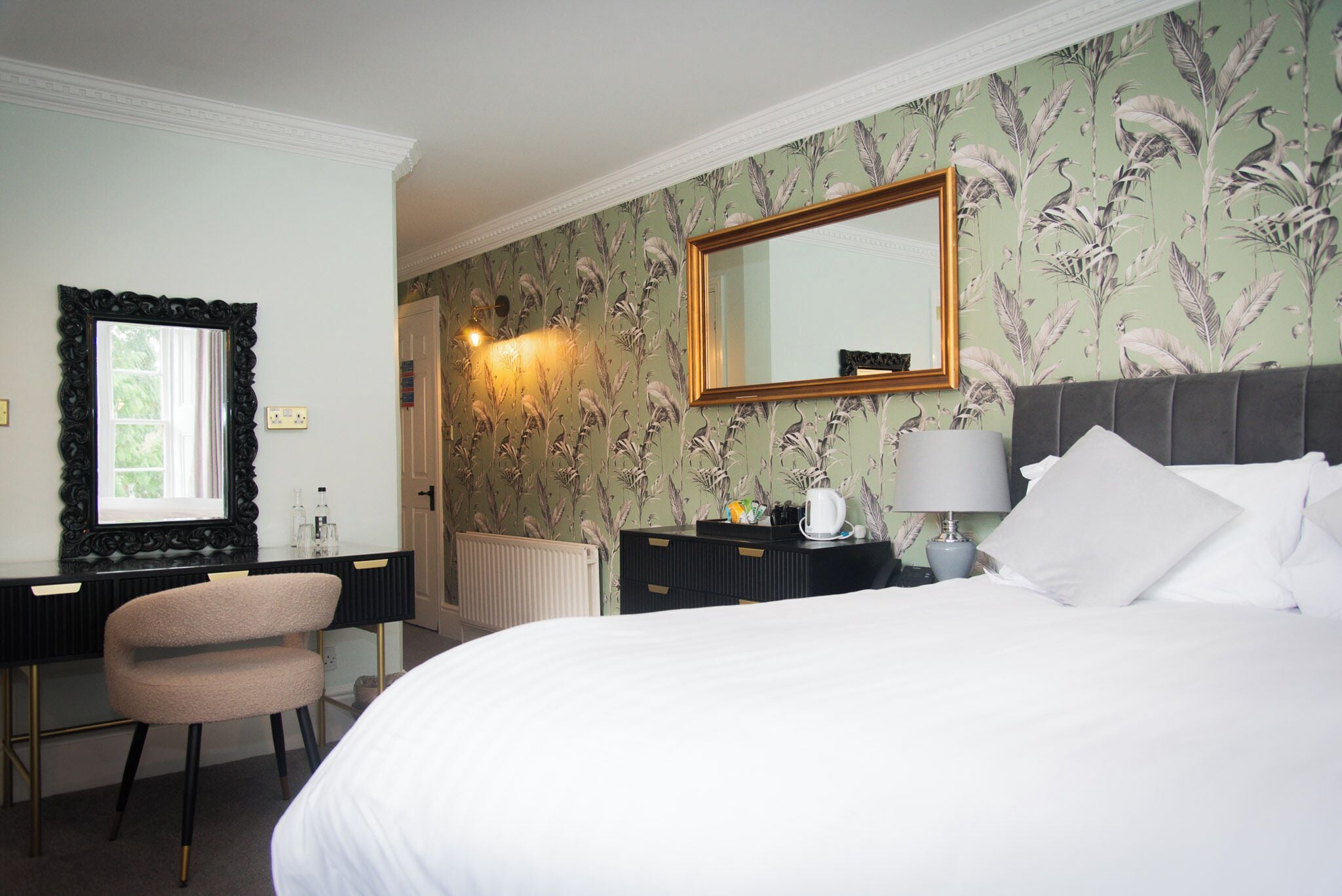 A hotel room with a bed, a desk, a chair, a dresser, a mirror, and a radiator.