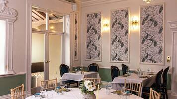A dining room with a chandelier, white tablecloths, and wooden chairs.