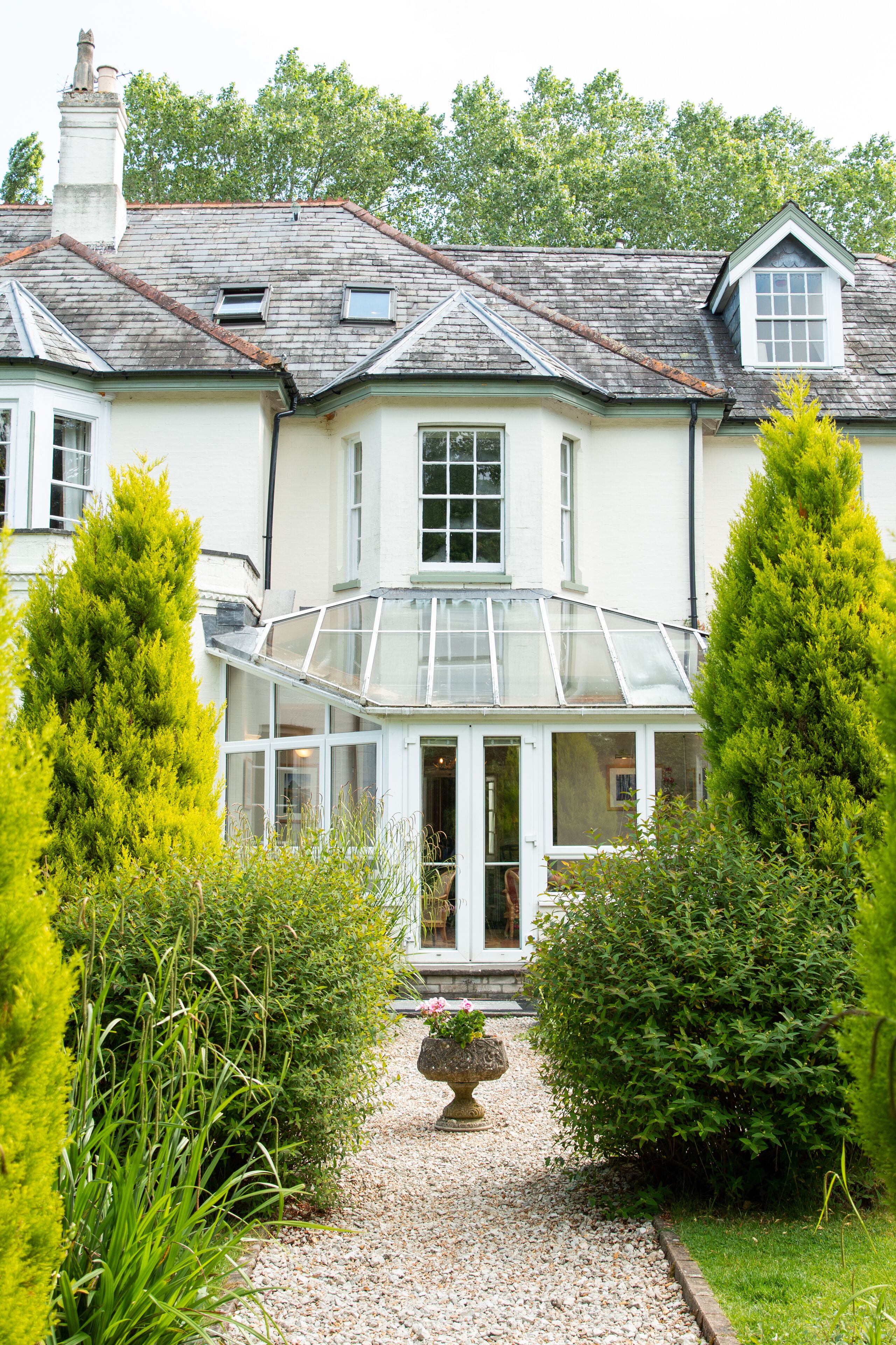 Une maison dotée d’une véranda, entourée de verdure et bordée d’un chemin de gravier.