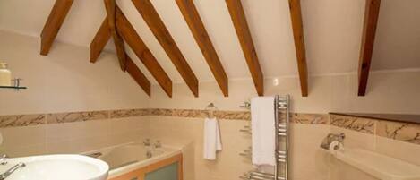 A bathroom with a bathtub, a sink, and a toilet. There are wooden beams on the ceiling, and a towel rack is visible.