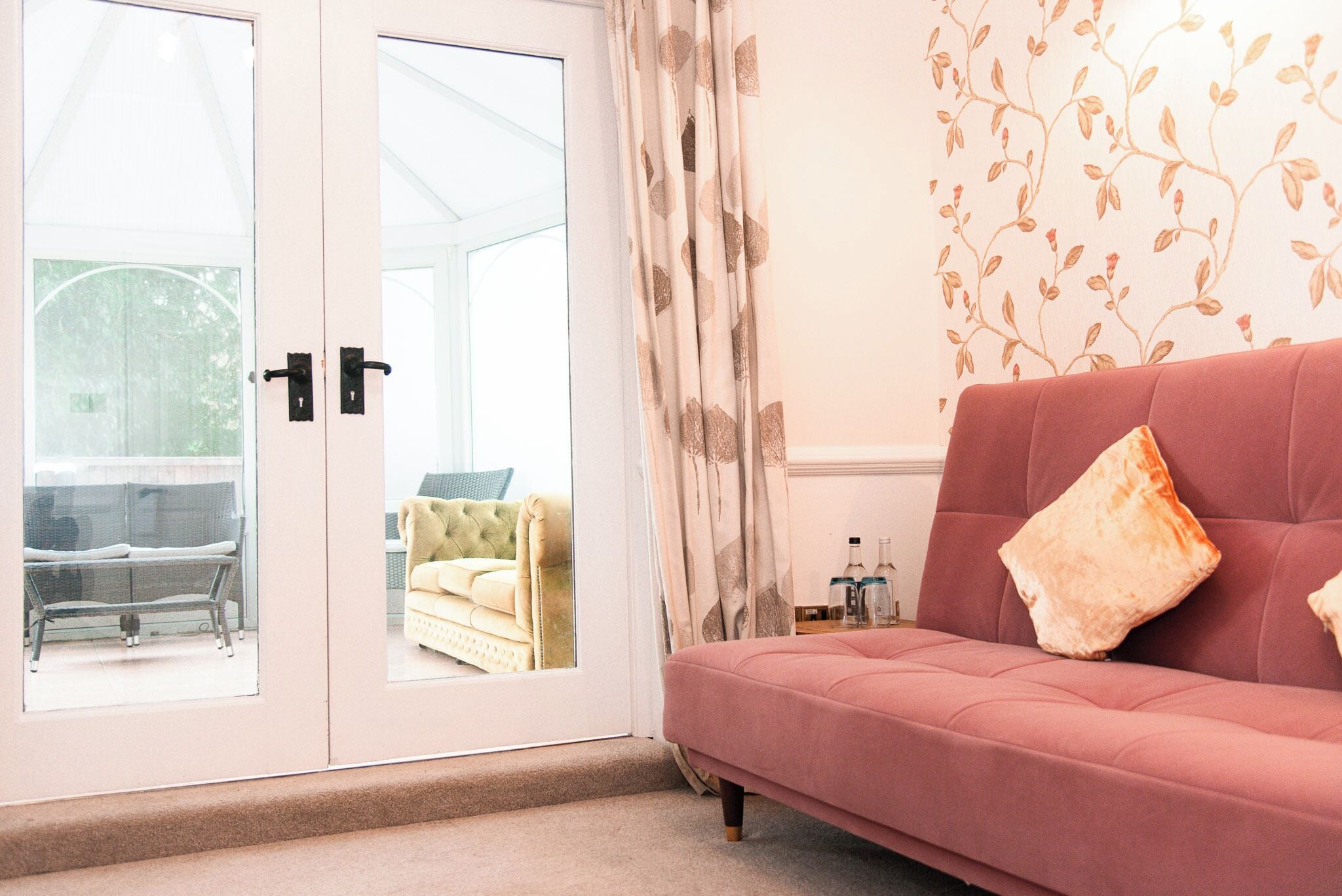 A room with a pink sofa, a glass door leading outside, and a wall with a leaf pattern.