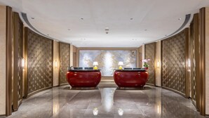 A spacious lobby with a polished marble floor, two red reception desks, and a large decorative wall with a floral pattern. - Landmark International Hotel (Guangzhou)