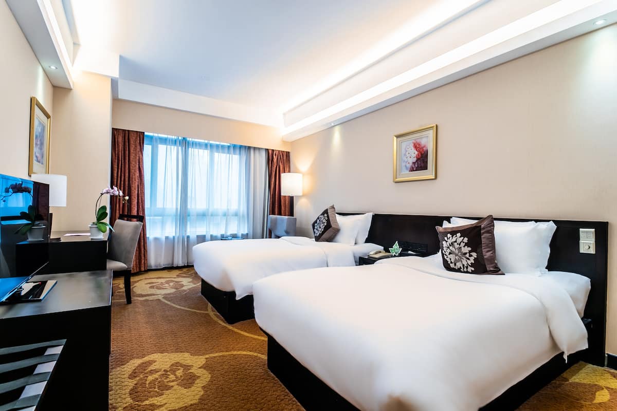 Een hotelkamer met twee bedden, een bureau, een stoel, een lamp en een raam met gordijnen.