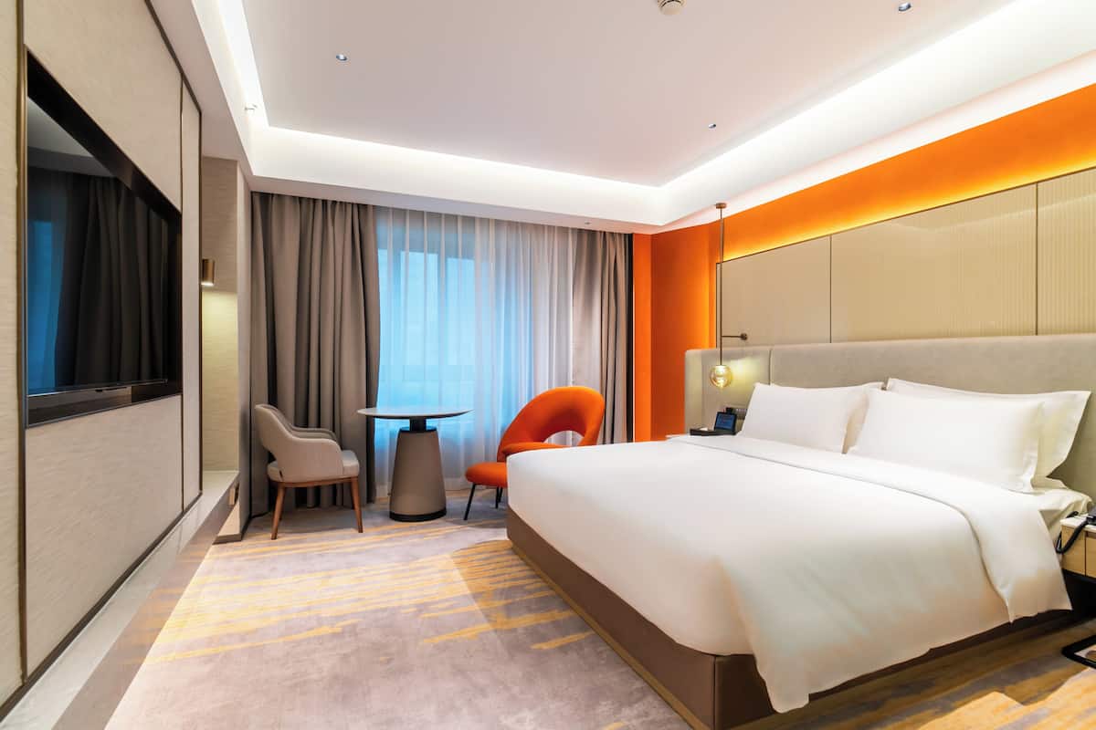 Een hotelkamer met een groot bed, een bureau, twee stoelen, een raam met gordijnen en een aan de muur bevestigde televisie.