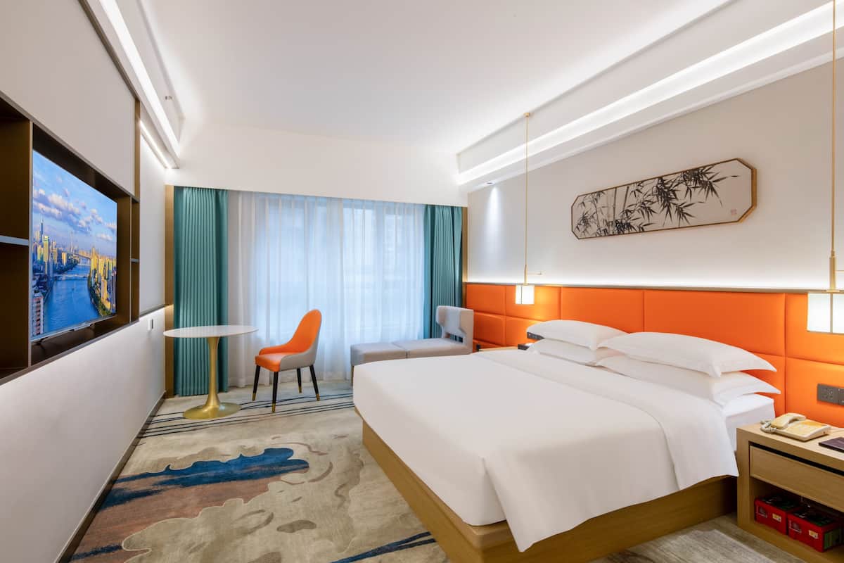 Een hotelkamer met een bed, een bureau, een stoel, een televisie en een schilderij aan de muur.