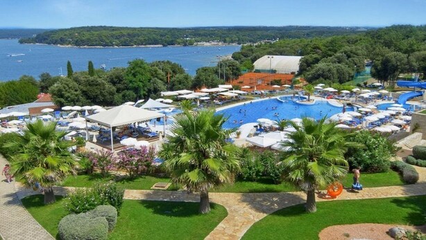 A resort with a large swimming pool, palm trees, and a view of the sea. - Valamar Tamaris Villas (Tar-Vabriga)
