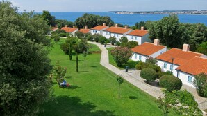 A coastal residential area with white buildings and red roofs, a paved walkway, and a view of the sea. - Valamar Tamaris Villas (Tar-Vabriga)