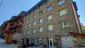 A multi-story hotel with stone facade, multiple windows, and a parking area. - Somriu Hotel Vall Ski (Soldeu)