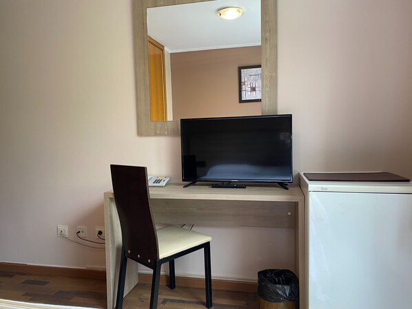 A room with a wooden desk, a television, a chair, a small trash bin, and a refrigerator. - Somriu Hotel Vall Ski (Soldeu)