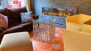 A living room with a stone fireplace, a sofa, a yellow armchair, and a patterned ottoman. - Somriu Hotel Vall Ski (Soldeu)