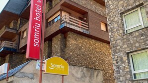 A hotel with a stone facade, multiple balconies, and a red sign indicating the name "Somriu hotel". - Somriu Hotel Vall Ski (Soldeu)