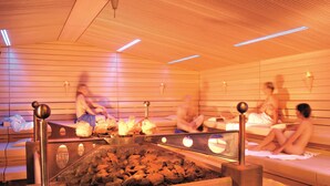 Una sauna con paredes y bancos de madera, un suelo central de piedra climatizada e iluminación en el techo.