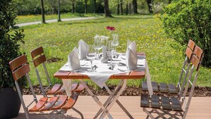 Un espace de restauration en plein air avec une table dressée pour quatre personnes, entourée de chaises, dans un cadre de jardin.