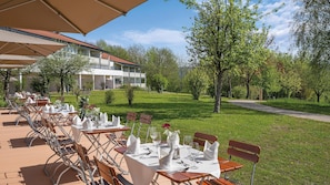 An outdoor dining area with tables set for guests, surrounded by trees and a building in the background. - Best Western Aparthotel Birnbachhoehe (Bad Birnbach)