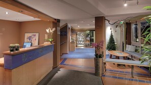 En hotellobby med en receptionsdisk, en sittgrupp med bord och stolar samt en trappa som leder till ett annat våningsplan.