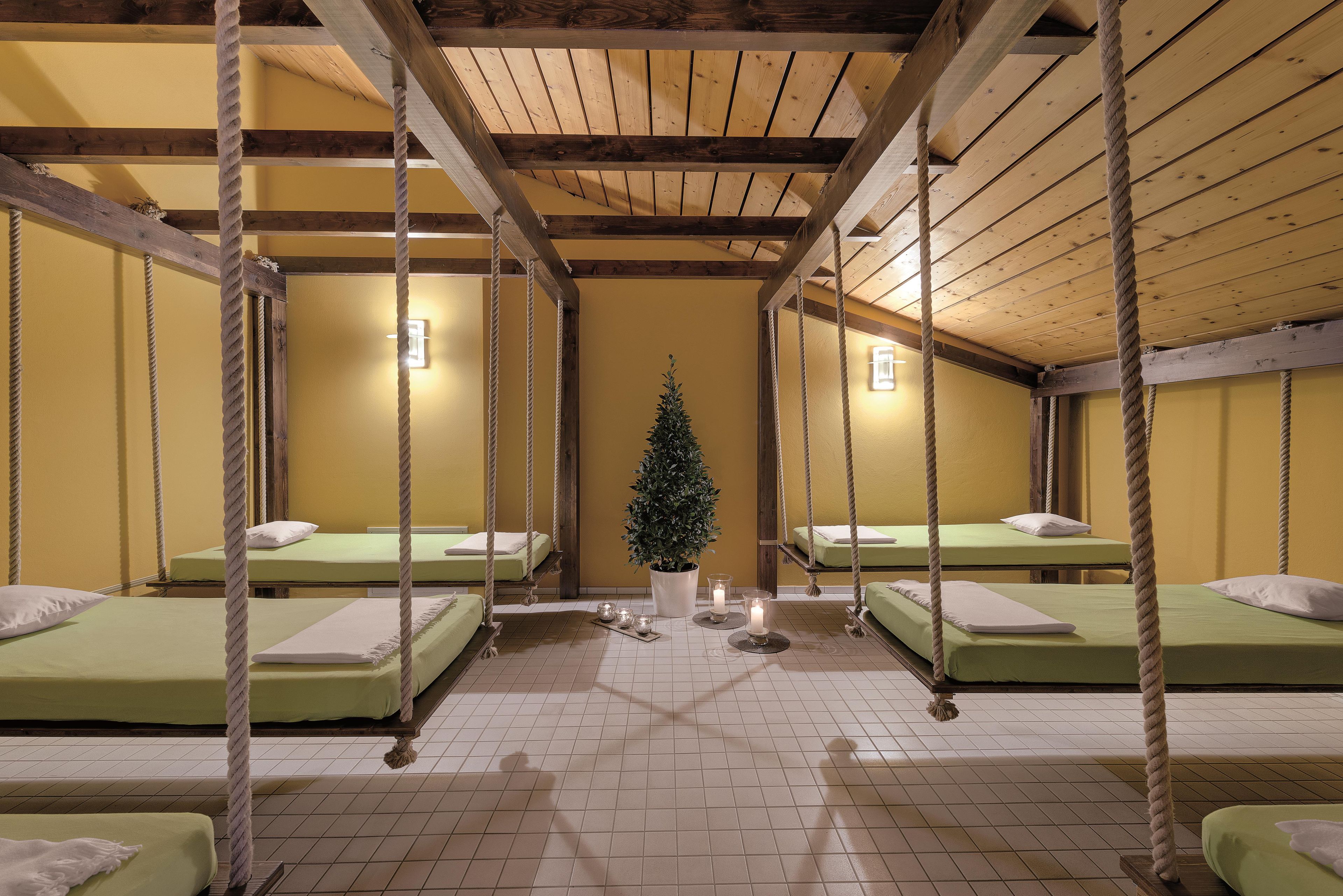 A room with four beds suspended from wooden beams, a central potted plant, and a tiled floor.