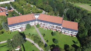 A large, modern building with a red roof, surrounded by green lawns and trees. - Best Western Aparthotel Birnbachhoehe (Bad Birnbach)