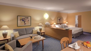 Une chambre d’hôtel avec un canapé, un bureau en bois, un lit et une table à manger avec des fruits.