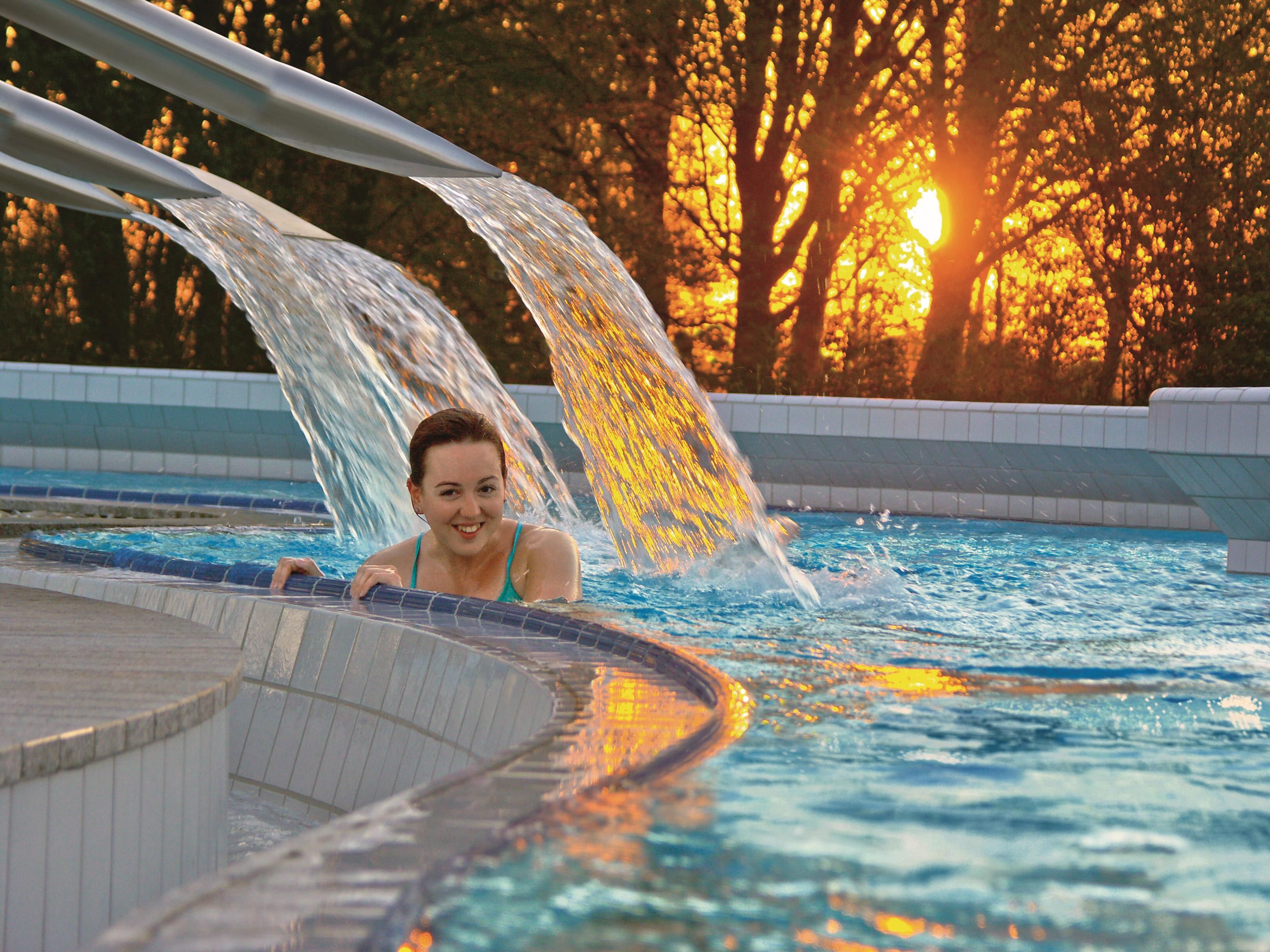 Una piscina con fuente de agua y una puesta de sol al fondo.