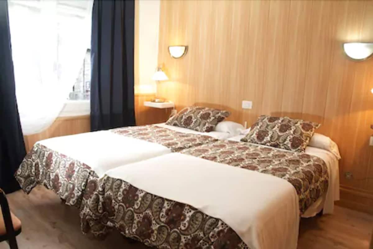 A double bed with patterned bedding, bedside lamps, and a wooden headboard.