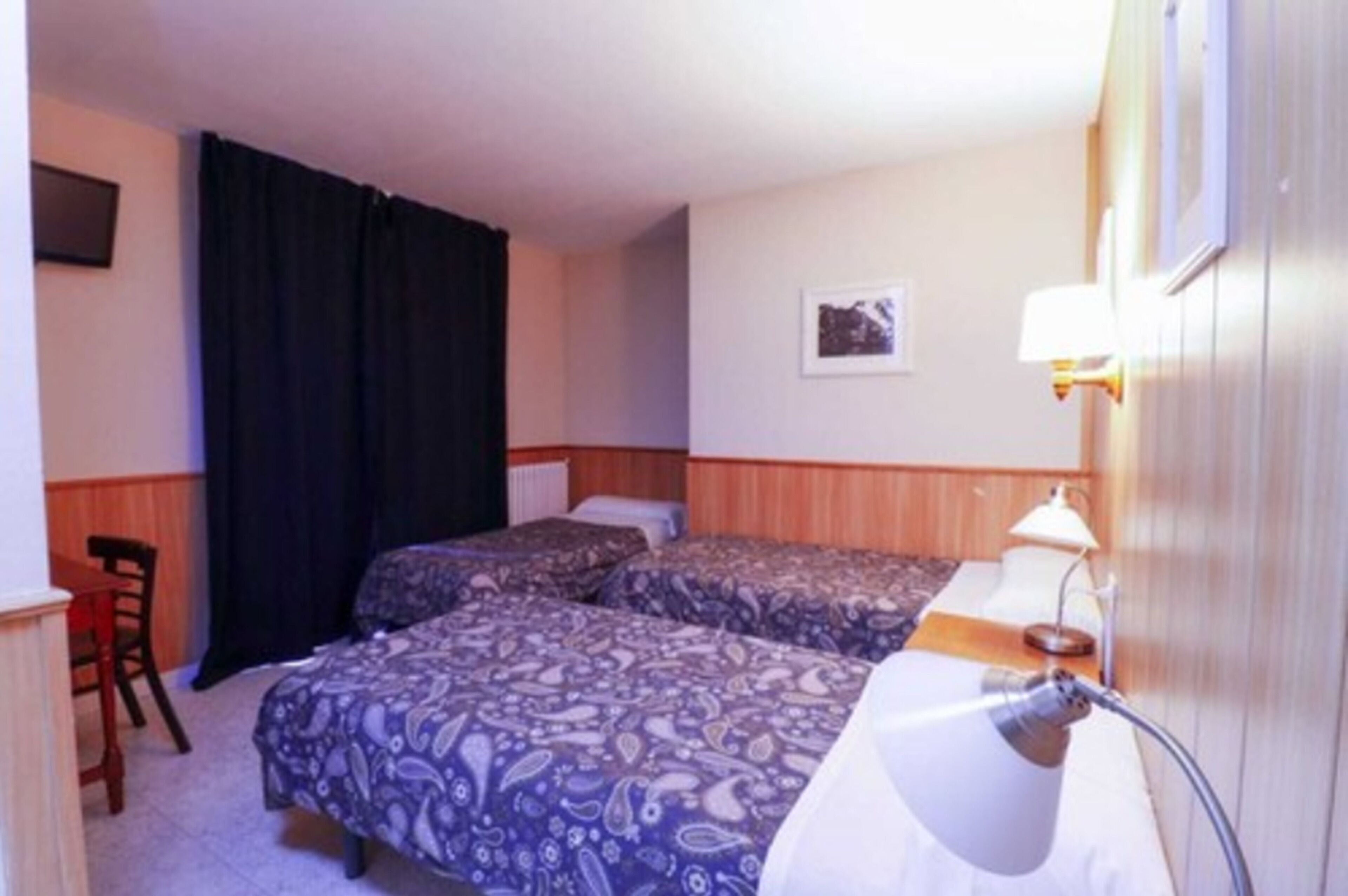 A hotel room with two beds, a desk, a chair, a lamp, and a picture on the wall.