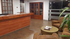 A reception area with a wooden reception desk, a seating area with brown leather chairs, a round coffee table, and a large window with a view. - Hotel Comapedrosa (Arinsal)