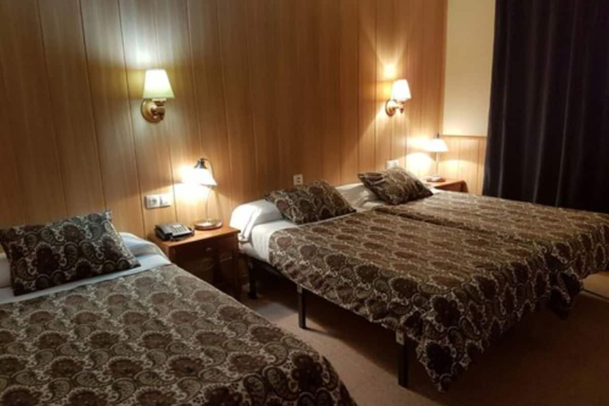 A hotel room with two single beds, wooden paneling on the walls, and bedside lamps.