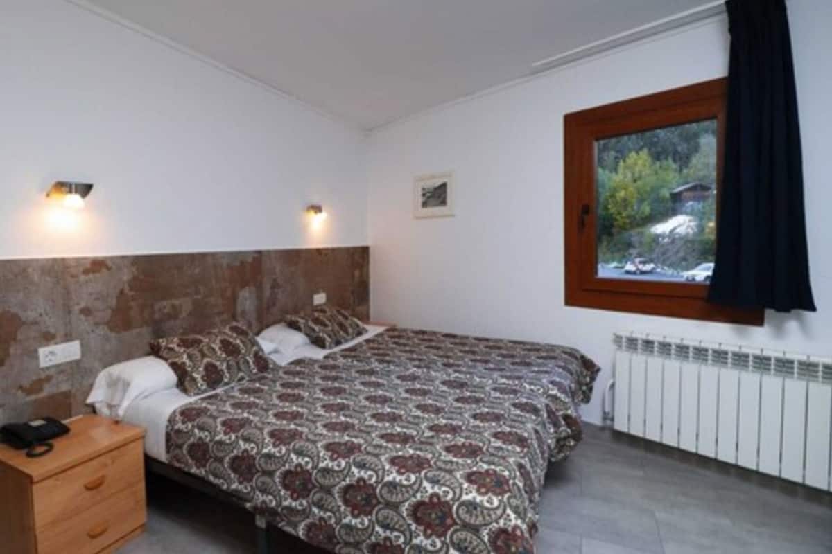 A bedroom with a bed, bedside table, and a window with a view of trees.