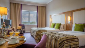 Habitación de hotel con dos camas, zona de comedor con desayuno, ventana grande y vistas al exterior.