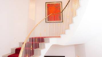 A spiral staircase with a red carpet, white walls, and framed artwork.