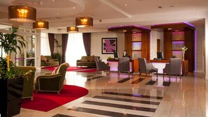 Un vestíbulo de hotel con recepción, zona de estar y grandes ventanales.